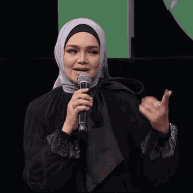 a woman in a hijab holds a microphone in her hand