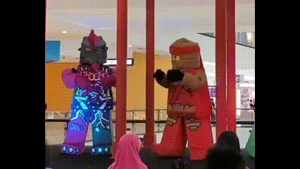 two lego characters are standing next to each other in front of a crowd of people in a mall .