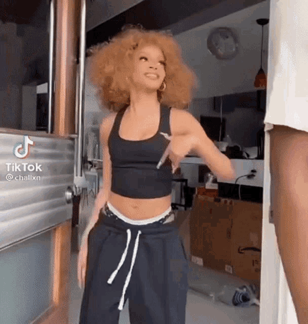 a woman with red hair is standing in front of a door wearing a black crop top and black sweatpants .