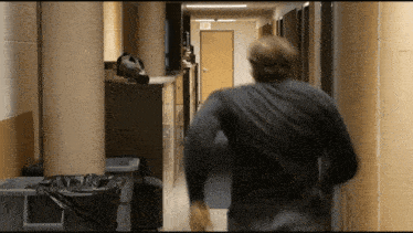 a man in a black shirt is running down a hallway with an exit sign on the door