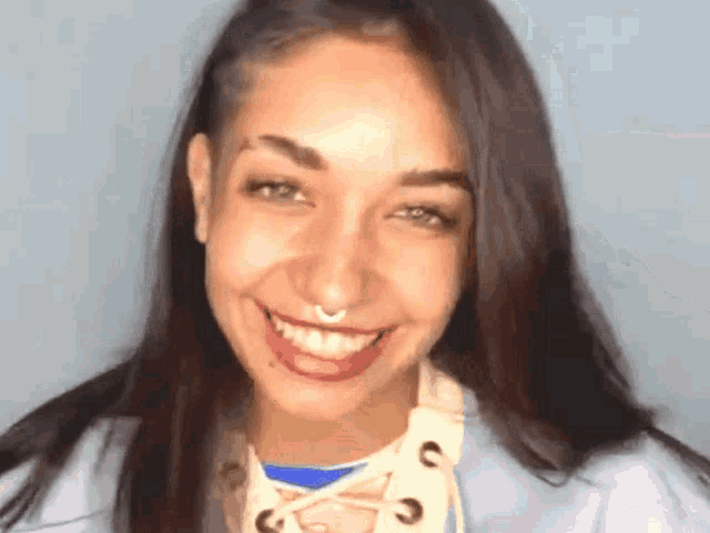 a woman with a nose ring is smiling and wearing a lace up top