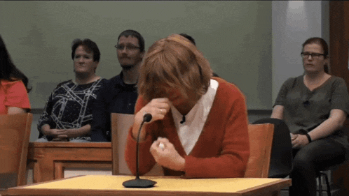 a woman in a red sweater sits at a table with a microphone