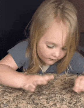 a little girl in a blue shirt is sitting on a counter