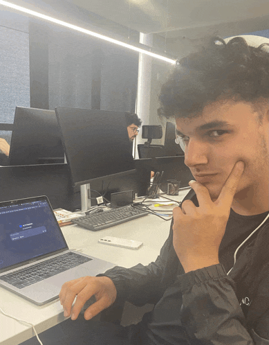 a man sitting at a desk with his hand on his chin looking at his laptop