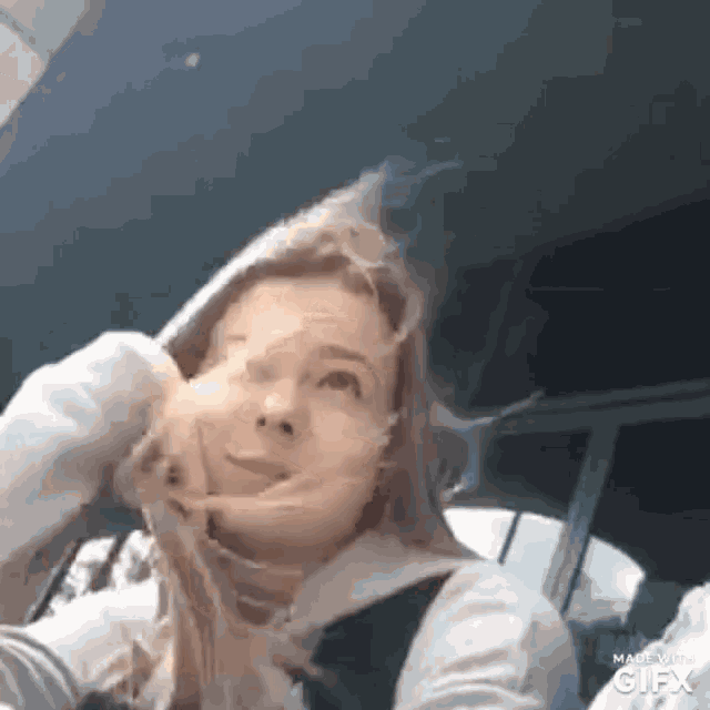 a woman is making a funny face in a car while wearing a hoodie .