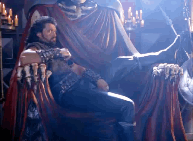 a man sitting on a throne with a statue behind him