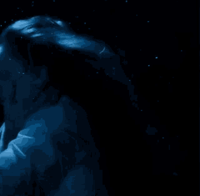 a woman is swimming underwater in a dark room with her hair blowing in the wind .