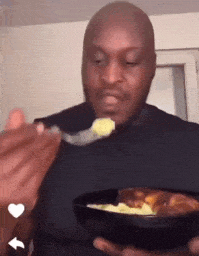 a man in a black shirt is eating food from a bowl with a spoon .