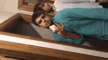 a man in a blue shirt is taking a picture of himself in a coffin .