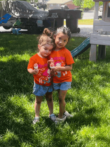 two little girls are standing in the grass wearing orange shirts that say mom