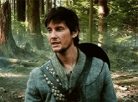 a man with a backpack is standing in the woods .