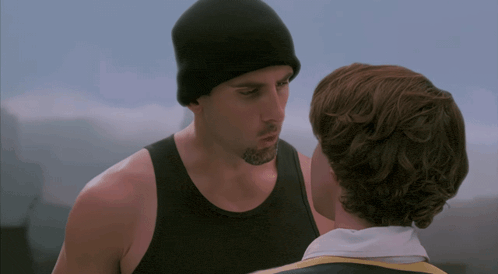a man wearing a black tank top and a black beanie looks at another man