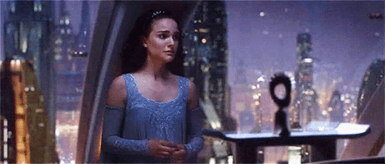 a woman in a blue dress is standing in front of a window in a room with a city in the background .