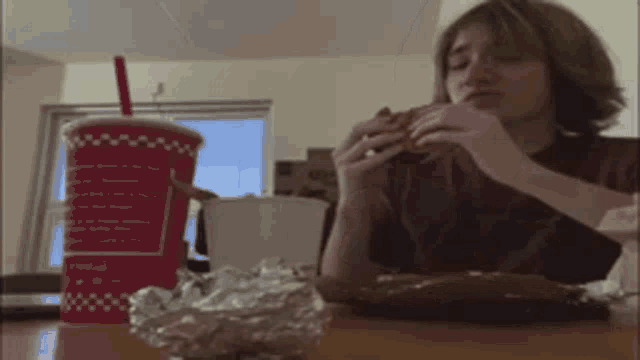 a person is sitting at a table eating a hamburger and drinking a coca cola