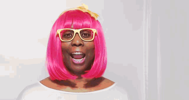 a woman wearing glasses and a pink wig is smiling