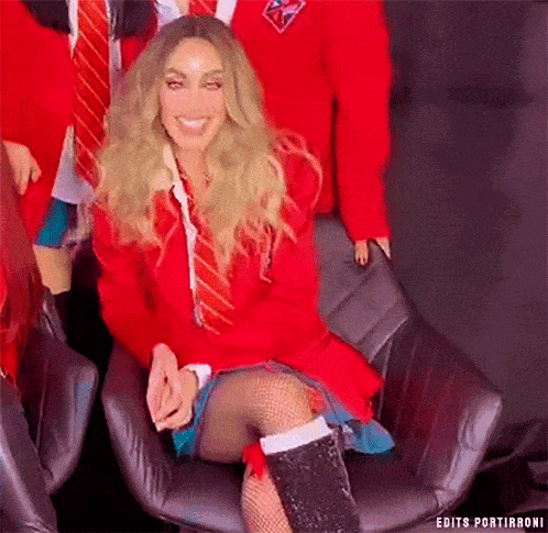 a woman in a red suit and tie is sitting in a chair with her legs crossed .