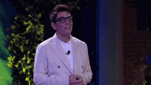 a man wearing glasses and a white suit is standing on a stage with a microphone .