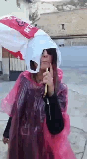 a woman wearing a pink plastic poncho with a bag on her head that says ' nln ' on it