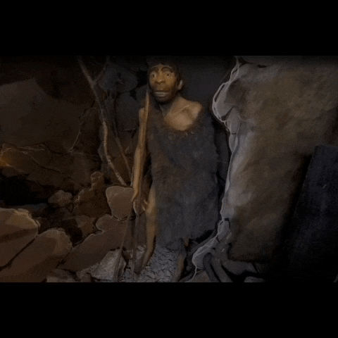 a statue of a caveman standing in a cave with a stick