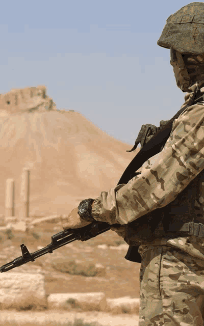a soldier in a camouflage uniform holds a gun in front of a mountain