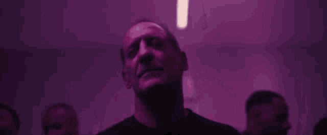 a man is standing in a dark room with purple lights looking up .