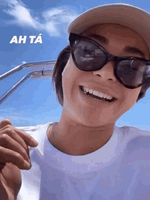 a woman wearing sunglasses and a hat is smiling with ah ta written above her