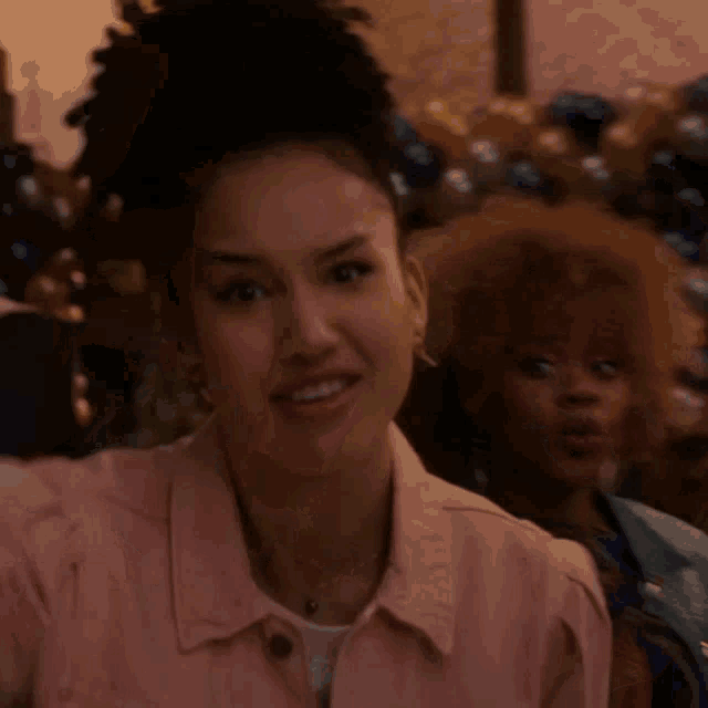 a woman in a pink jacket looks at the camera with balloons in the background