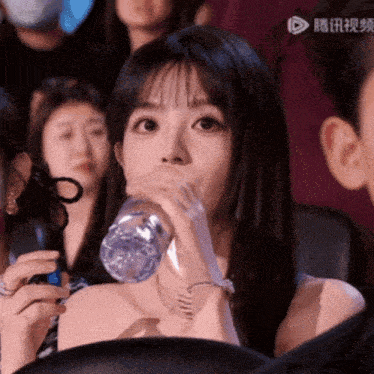 a woman drinking water from a plastic bottle with a ribbon around her neck