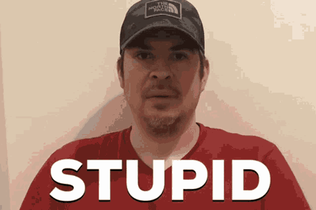 a man wearing a hat and a red shirt with the word stupid on it