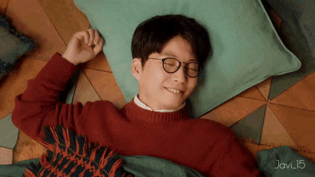 a man wearing glasses and a red sweater laying on a green pillow