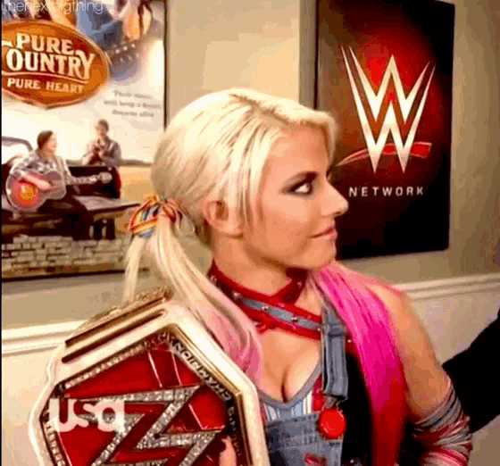 a woman is holding a wrestling championship belt in front of a wall with a wwe logo on it .