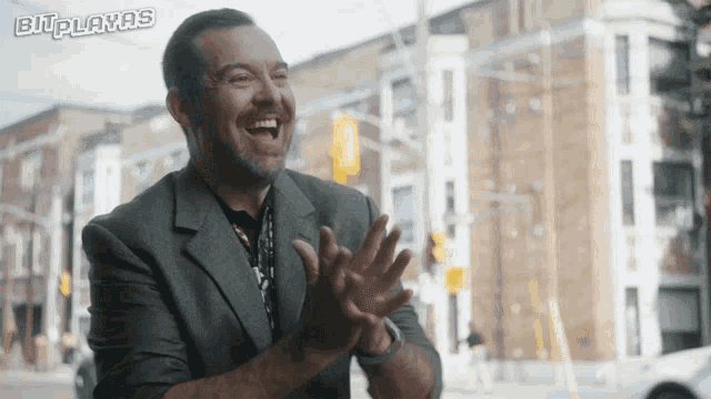 a man in a suit is clapping in front of a sign that says bit playas