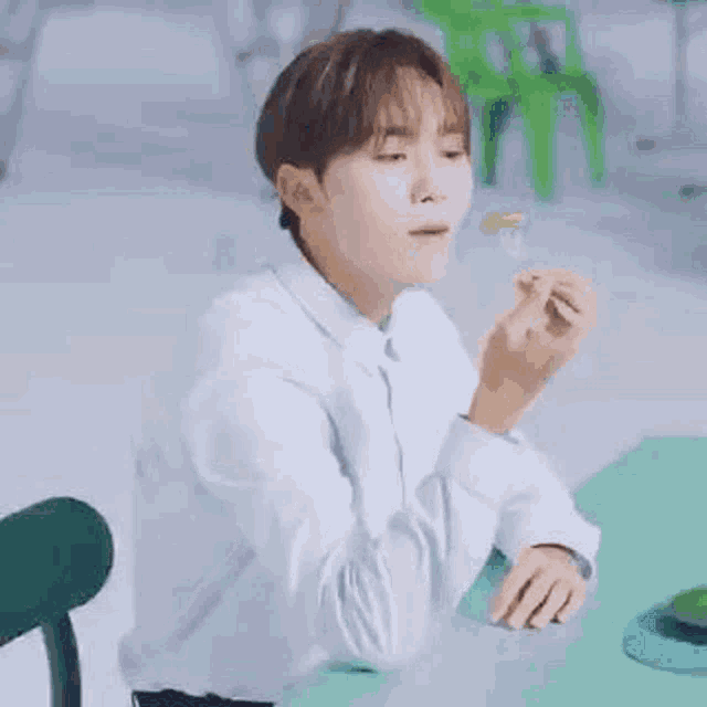 a young man in a white shirt is sitting at a table eating a green vegetable .