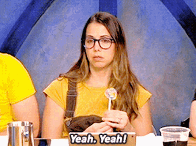 a woman sitting at a table holding a lollipop with a sign that says yeah yeah