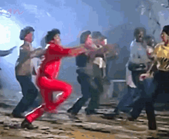a group of people are dancing in a dark room and one of them is wearing a red jumpsuit
