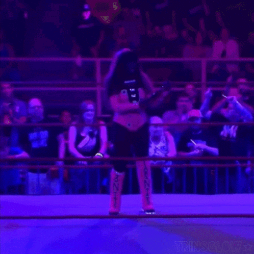 a wrestler is standing in a ring with a crowd watching .