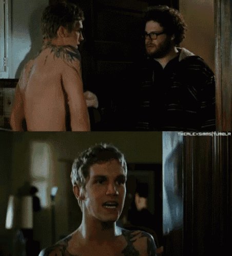 a shirtless man with a tattoo on his back stands next to another shirtless man with glasses