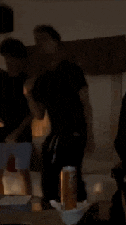 a man in a black shirt is dancing in a dark room with a can of beer in the foreground