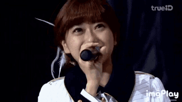 a woman is smiling while holding a microphone and the words imgplay are on the bottom right