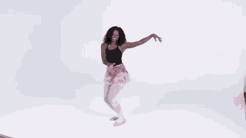 a woman in a black tank top and pink skirt is dancing .