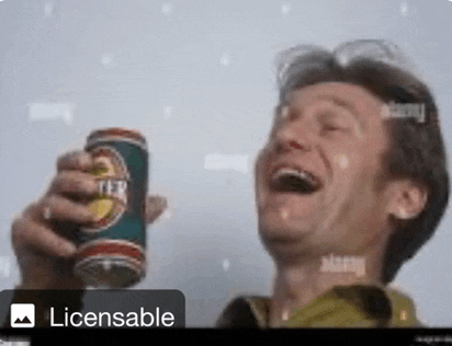a man is laughing while holding a beer can in his hand .