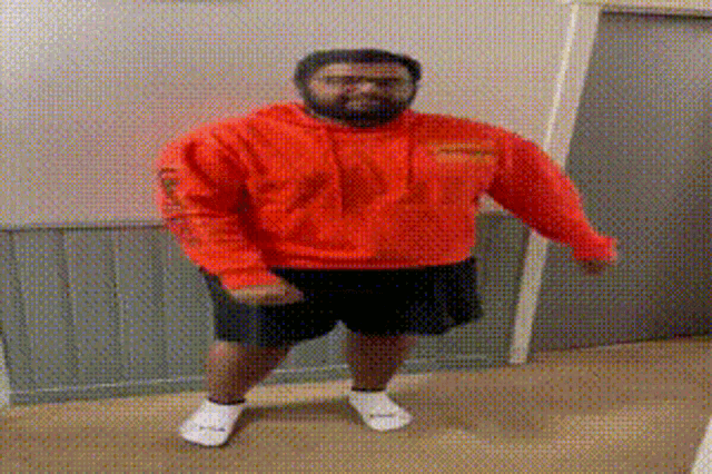 a man wearing an orange hoodie and black shorts is standing in a hallway