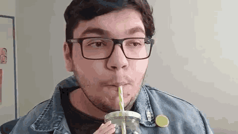 a man wearing glasses is drinking a smoothie through a straw .