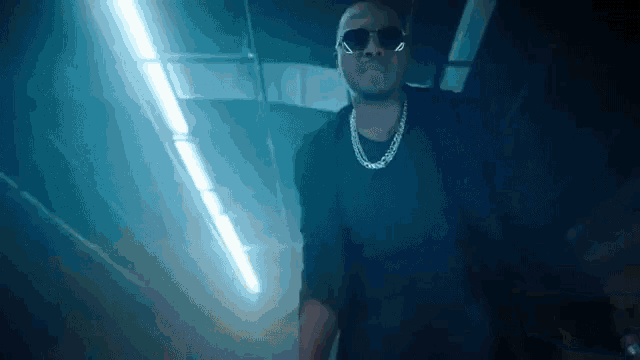 a man wearing sunglasses and a necklace is walking in a dark room .