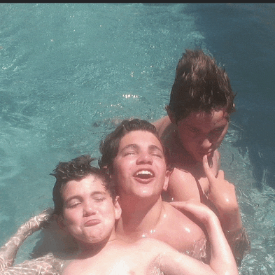 three young boys are swimming in a pool and one is making a funny face