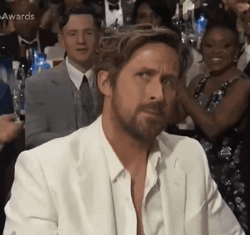 a man in a white suit is sitting in a crowd of people at an event .