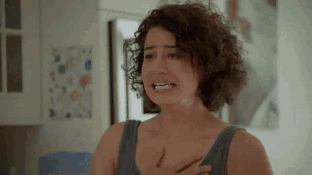 a woman with curly hair is crying with her hands on her chest .