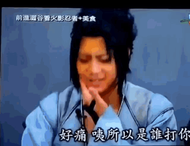 a man in a blue shirt is holding his face in pain