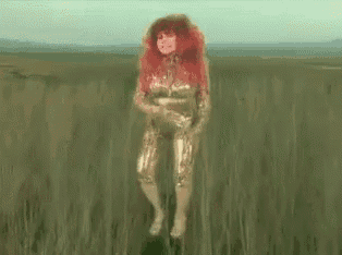 a woman with red hair is standing in a field with a blurred background .