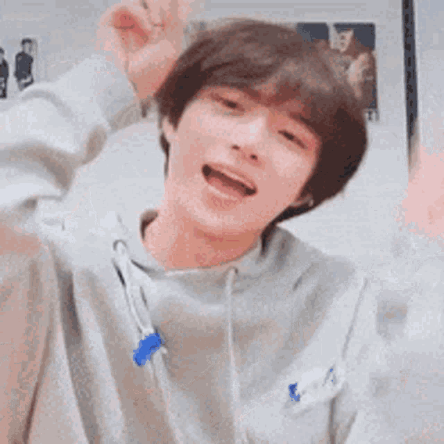 a young man wearing a gray hoodie is making a funny face and raising his hands in the air .
